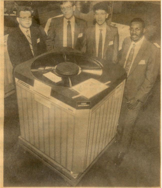 Newspaper photograph of four men standing beside a condensing unit at a trade show