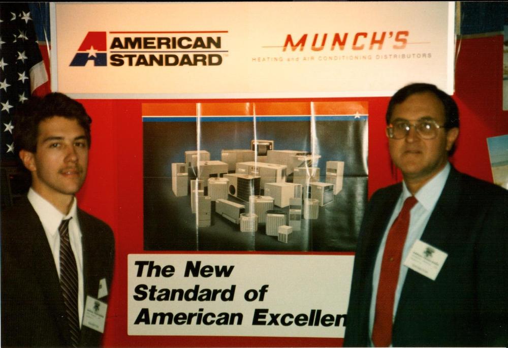 Two men at a trade show booth under American Standard and Munch's signage