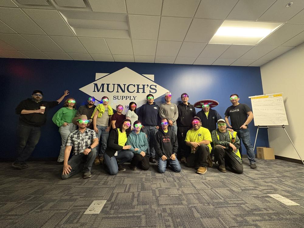 Branch and warehouse team posed in front of the Munch's Supply diamond painted on the wall