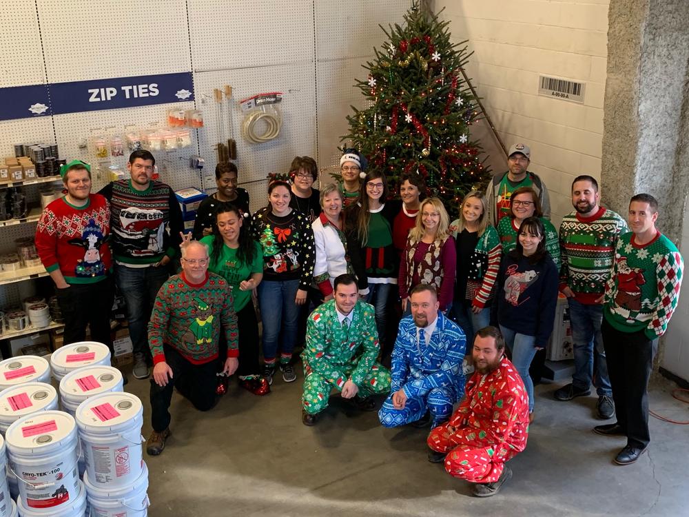 Office and warehouse team in holiday sweaters beside a decorated Christmas tree