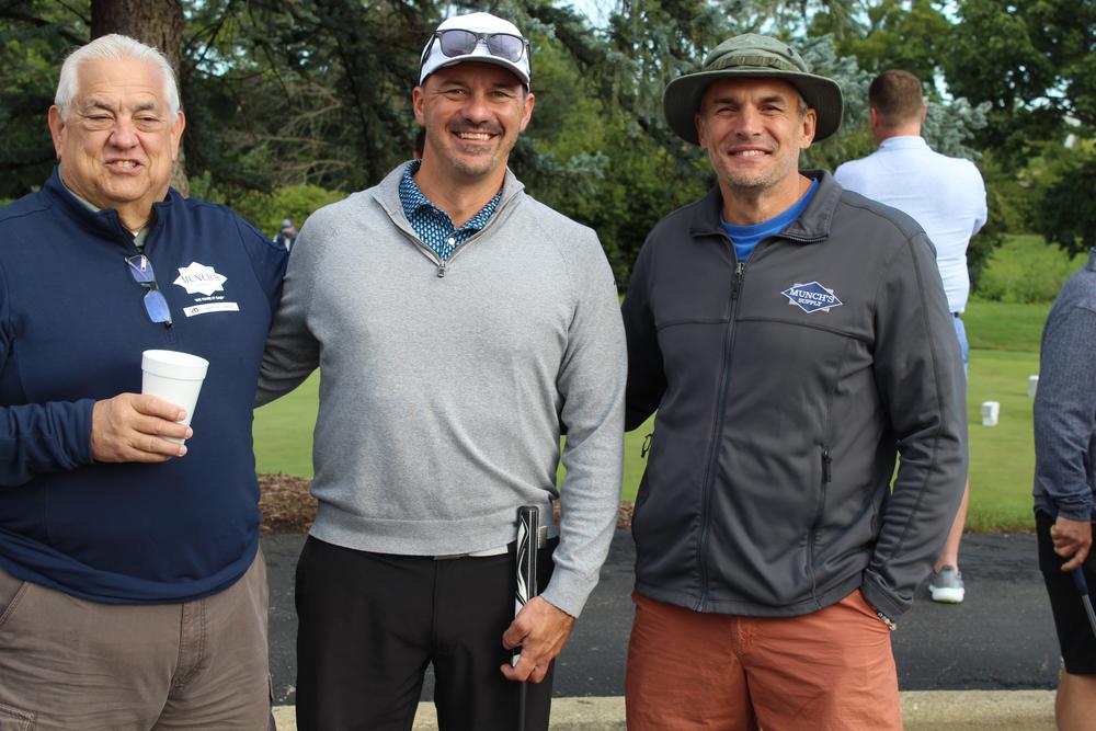 Three men in Munch's Supply jackets and pullovers on the course at the golf outing