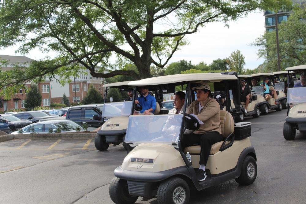 A line of golf carts rolling out of the clubhouse lot at the outing