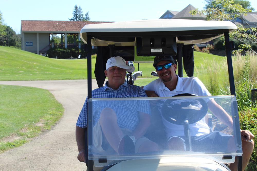 Two golfers in matching green shirts leading a line of carts down the cart path
