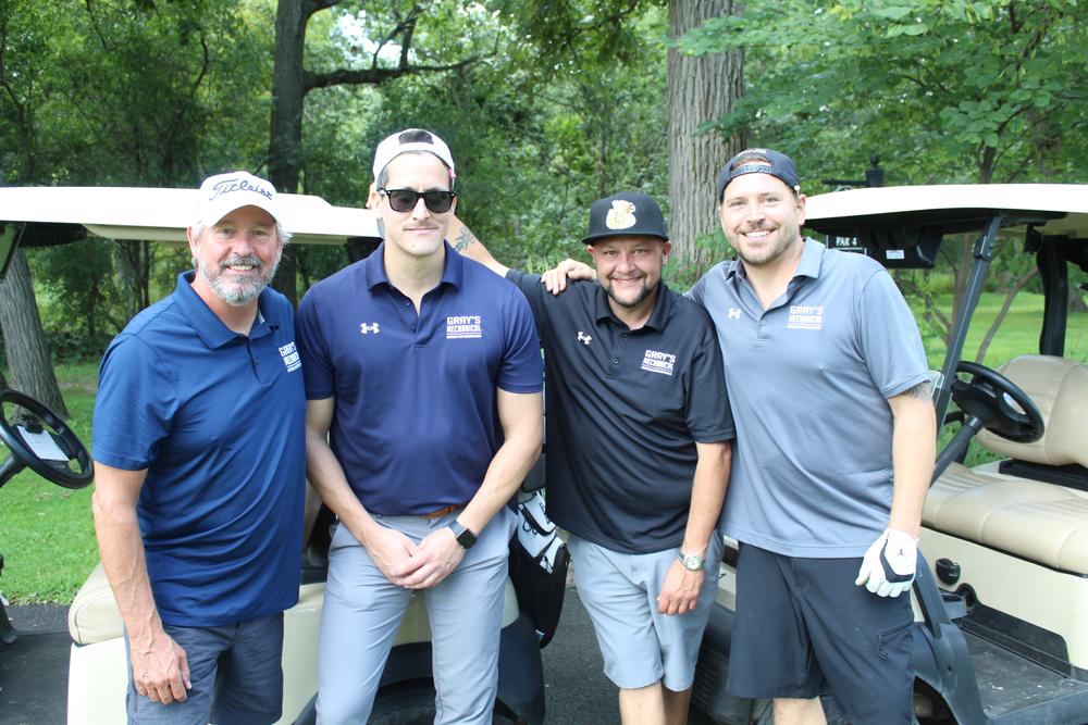 Four golfers in matching contractor polos standing beside a cart