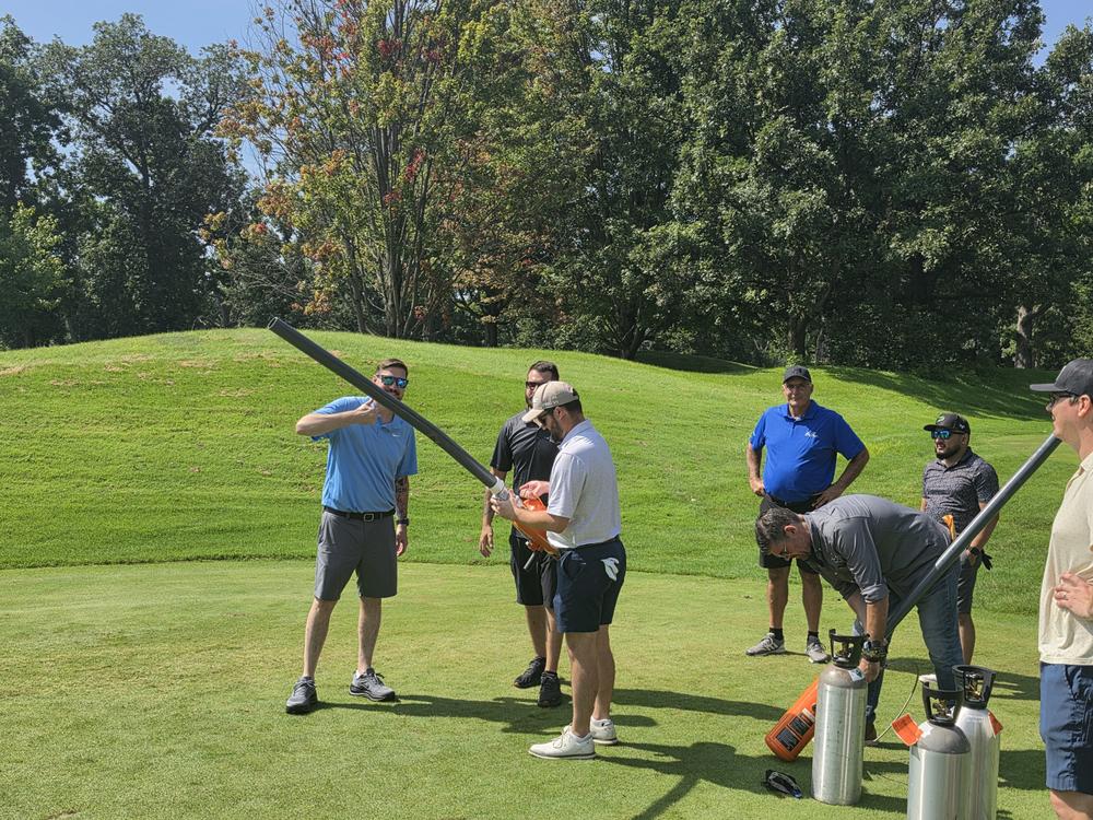Golfers loading a compressed air cannon on the course while others watch
