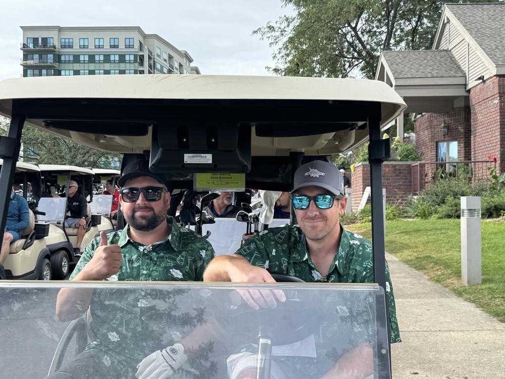 Two golfers in matching shirts giving a thumbs up from a golf cart