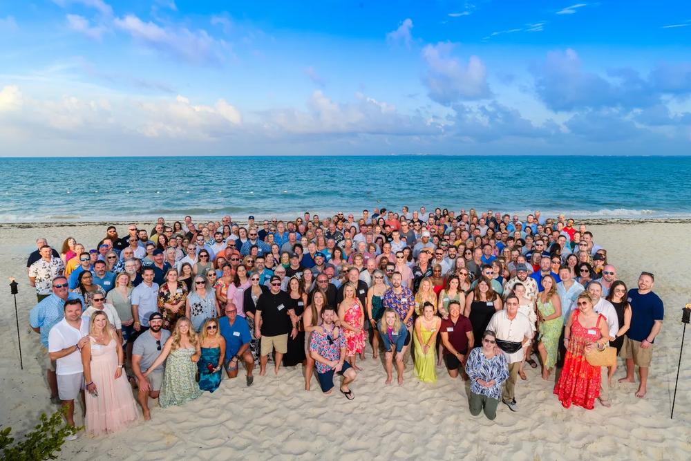Large dealer trip group photograph on a beach under a blue sky